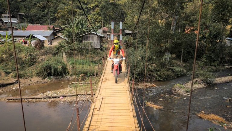 Rider riding over a bridge to cross a river in Loas.