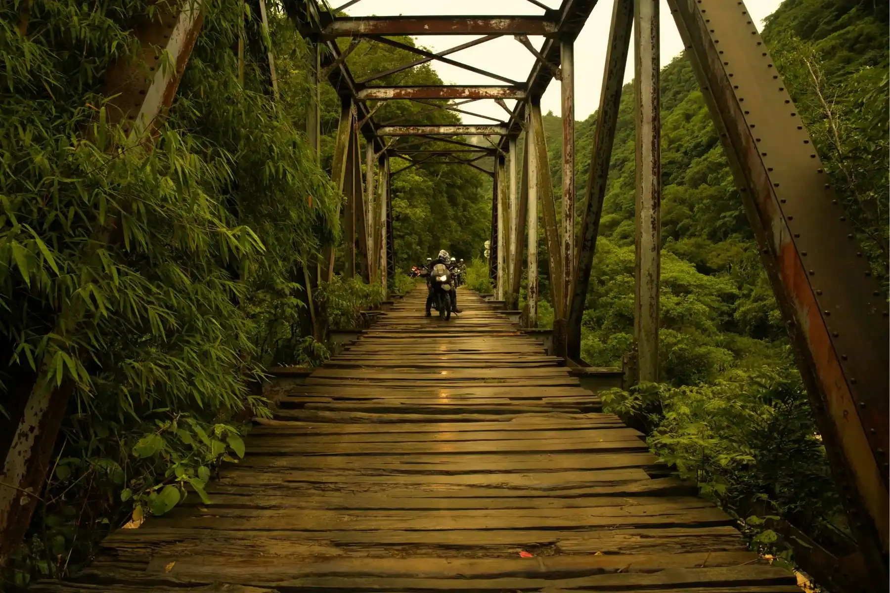 Motorcycle rider crossing an old bridge in the Colombian jungle on a trip to Colombia
