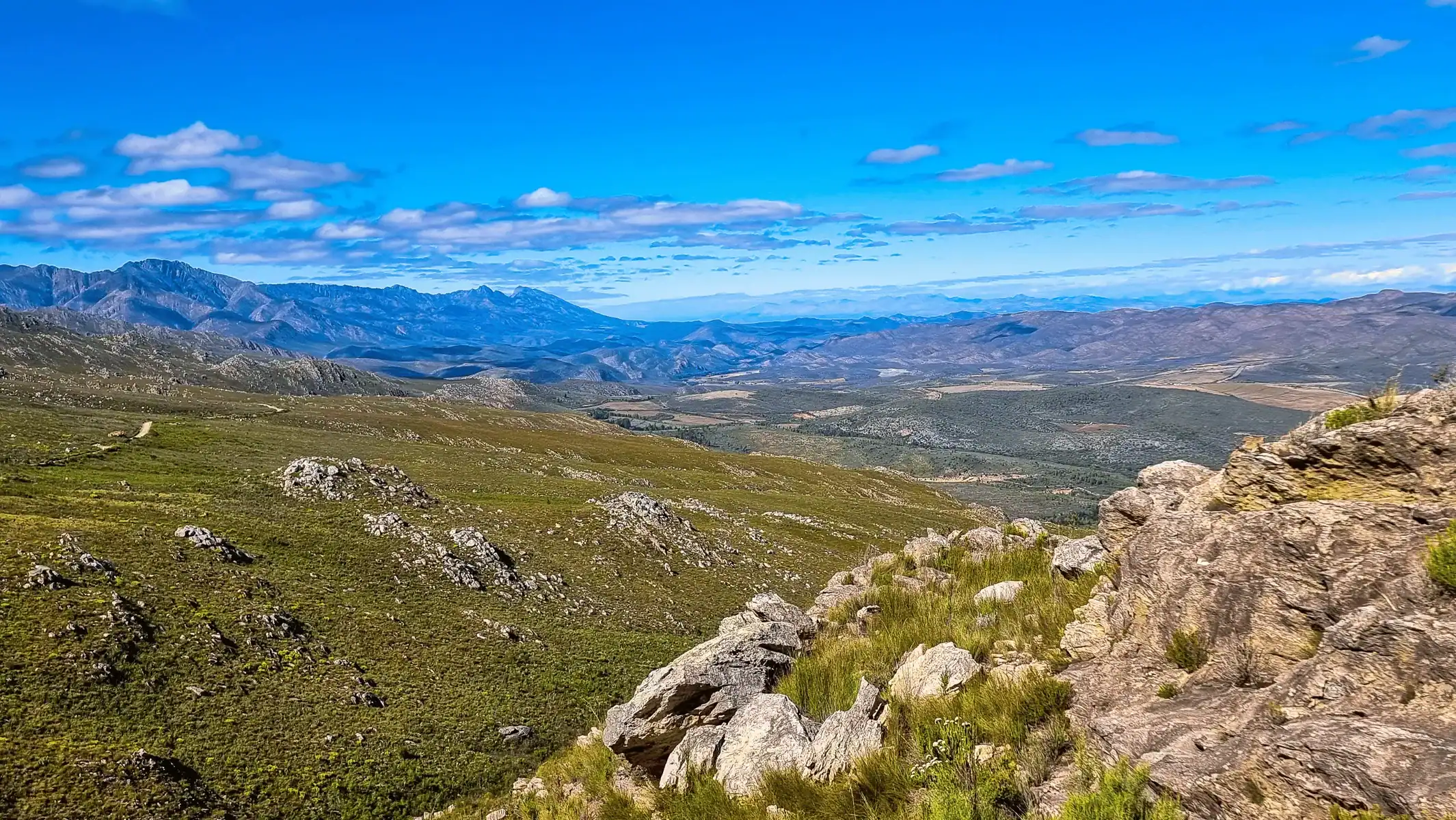 View over green hills and rocky outcrops towards distant mountain ranges