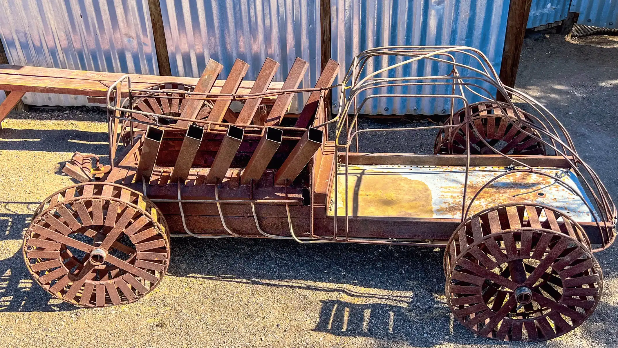 Wooden and wire-frame buggy sculpture in front of a corrugated metal wall