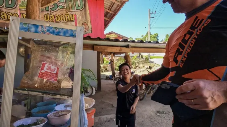 a dirt biker engaging with a local child in Thailand