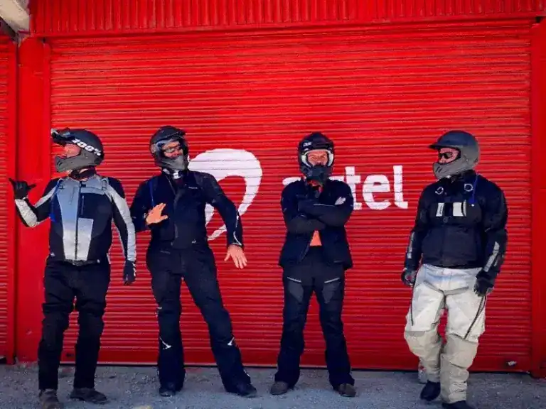 A group of riders standing in front of a red sign along the road in India