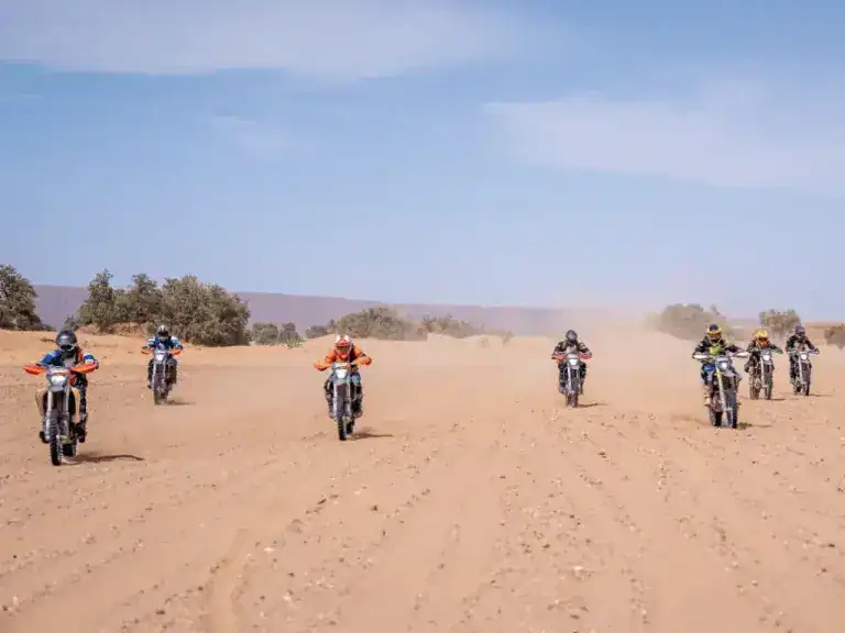 Riders cut across the open sands on a group dirt bike tour in Morocco.