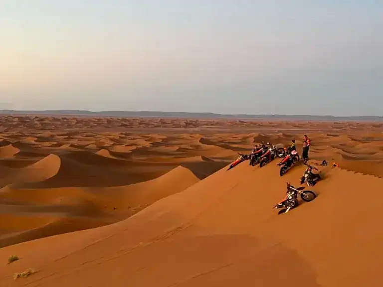 Motorcyclists watch the sun rise on the sand dunes in Morocco.