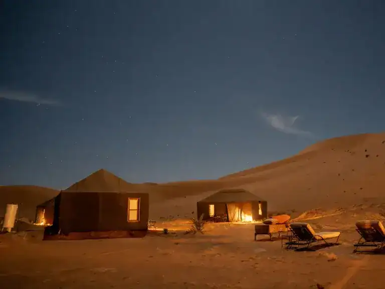 Sun set over warmly lit tents in the Moroccan dessert.