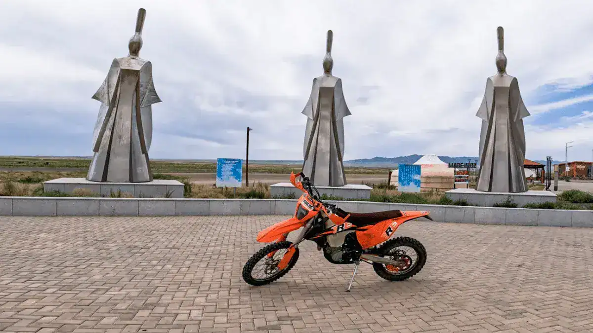 KTM 450 EXC parked in front of large statues in Mongolia